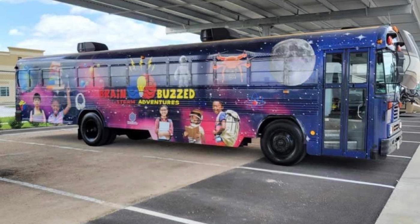 The BrainBuzzed Mobile STEAM Lab, a full-size bus in a space-themed wrap, parked at a Houston campus