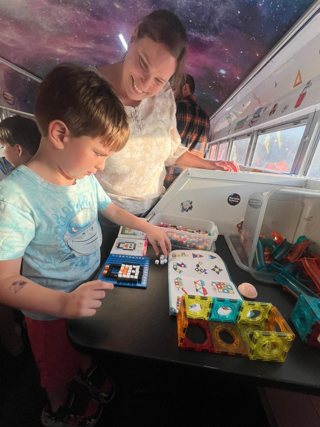 Inside the bus: a student and an instructor building with magnetic tiles beneath the galaxy ceiling
