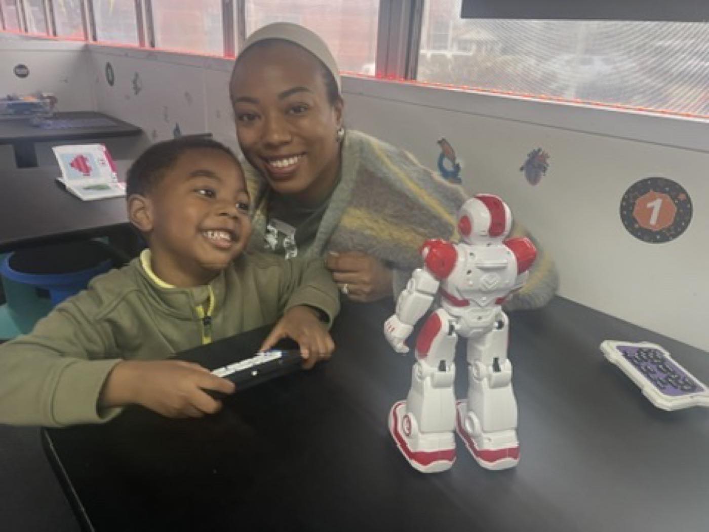 A parent and young student operating a robot together aboard the bus