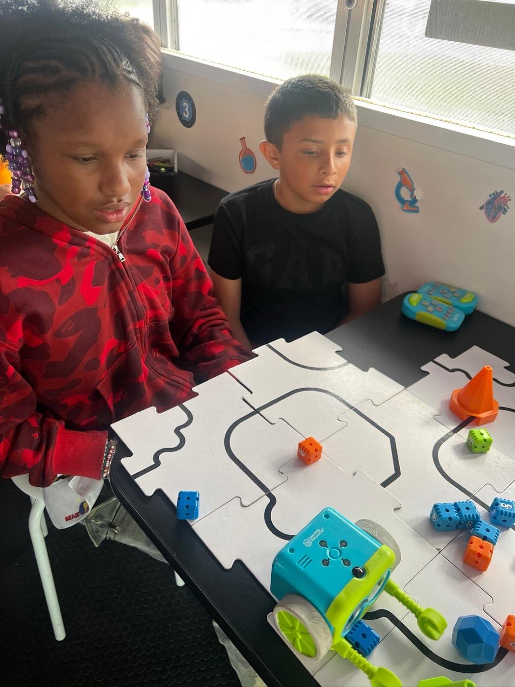 Two students guiding a coding robot around a track on the bench