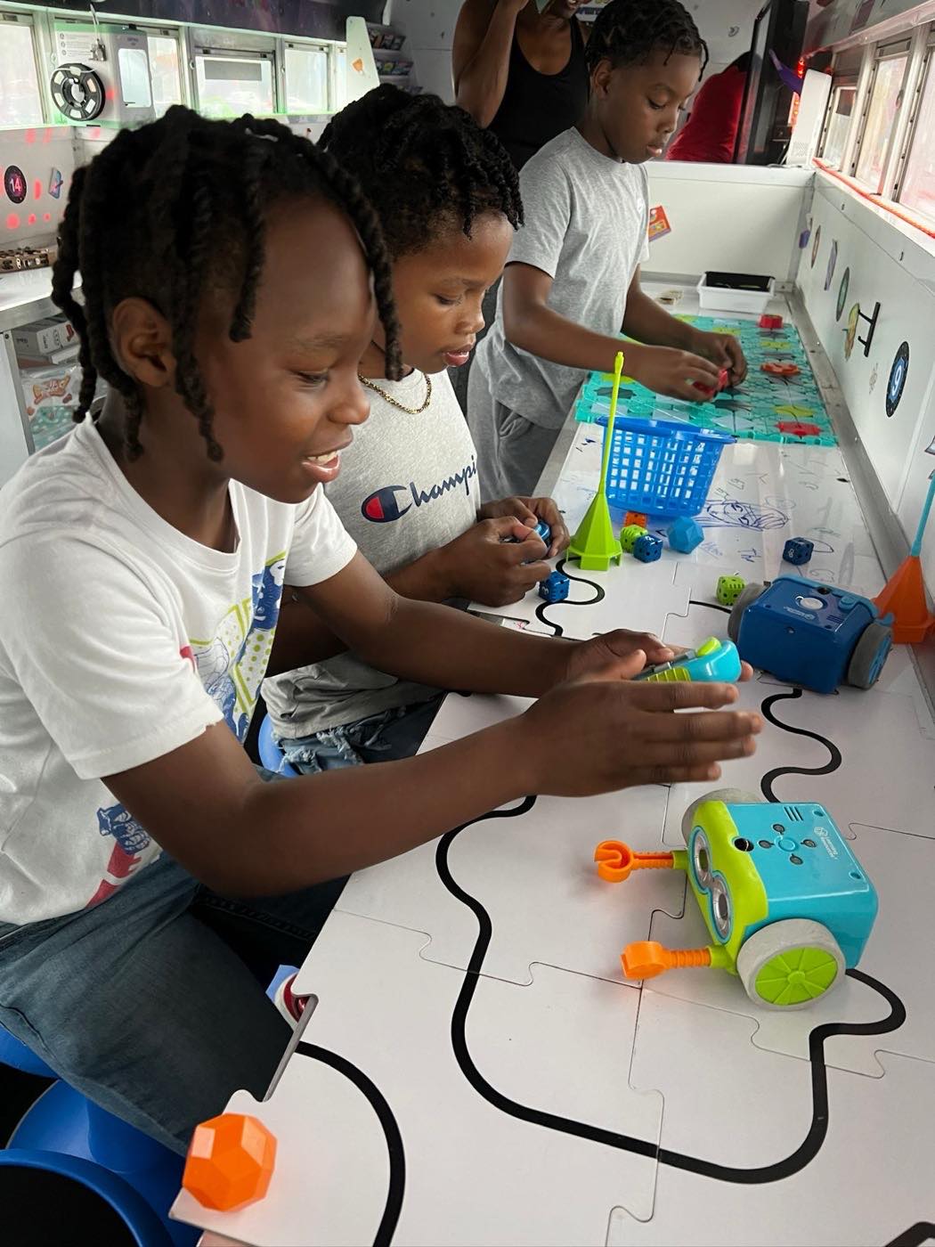Three students programming Botley coding robots along a track inside the bus
