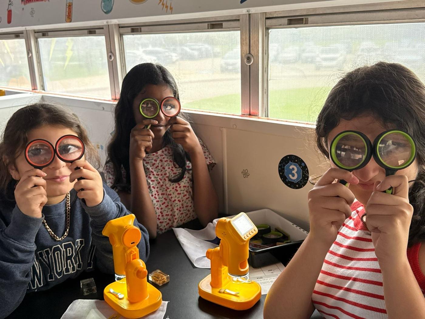 Three students holding magnifying lenses up to their eyes during a microscope activity